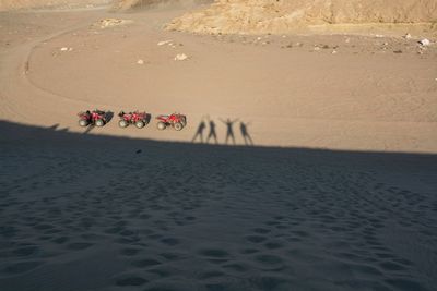 Shadow of people by quadbike on sand in desert during sunny day