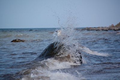 Waves splashing on shore against clear sky