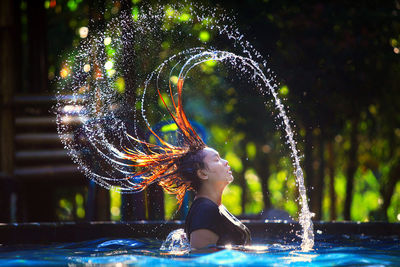 Side view of woman splashing water from hair in swimming pool