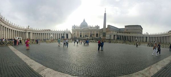 Tourists in front of building against cloudy sky