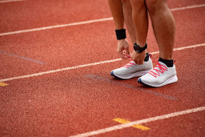 Low section of man tying shoelace while standing on running track