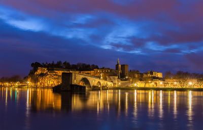 Illuminated bridge over river against cloudy sky