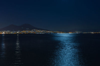 Illuminated city by sea against clear sky at night