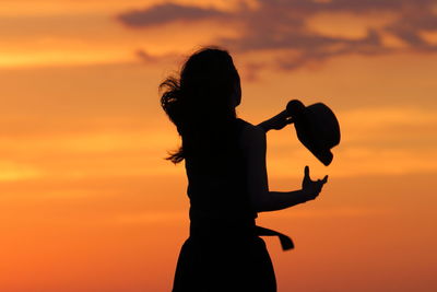 Silhouette woman standing against orange sky during sunset