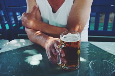 Midsection of man with drink sitting on table