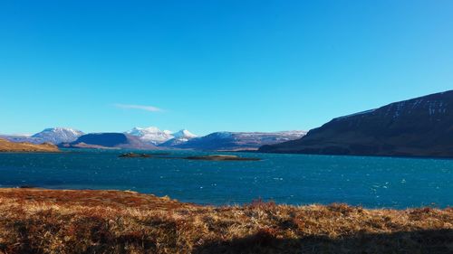 Scenic view of lake and mountains against clear blue sky