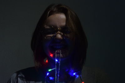 Portrait of woman holding illuminated lighting equipment against black background