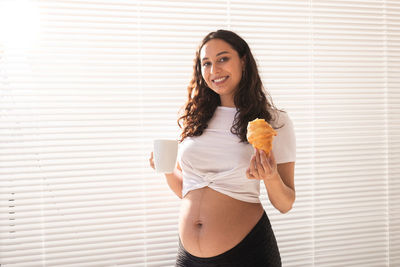 Young woman holding ice cream standing against wall