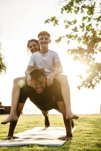 Father carrying children on back while practicing push-ups in park during sunset