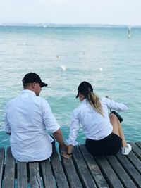 Rear view of couple sitting on pier over sea against sky