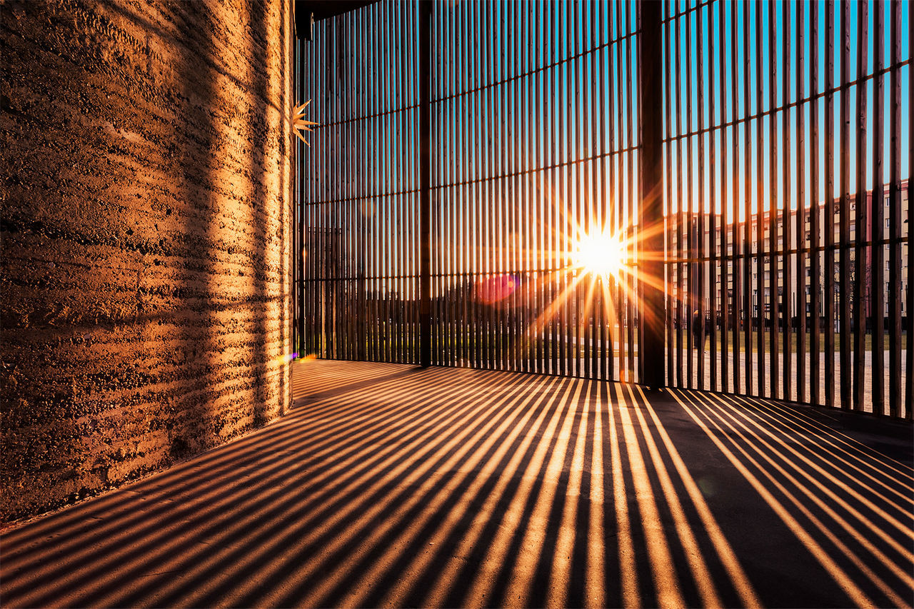 architecture, built structure, sunlight, building exterior, pattern, sun, sunbeam, sunset, indoors, window, lens flare, shadow, wall - building feature, glass - material, no people, the way forward, building, orange color, closed, metal grate