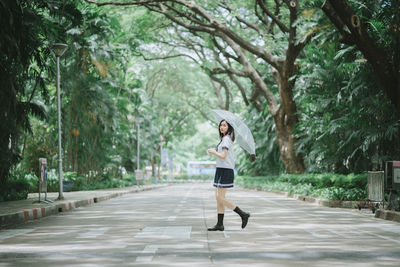 Portrait of young woman with umbrella walking on road