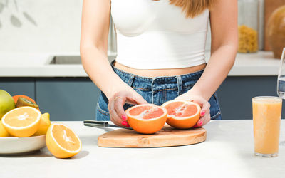 A woman cuts a juicy grapefruit on a cutting board in the kitchen surrounded by fresh fruit. 