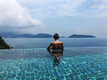 Rear view of woman in infinity pool against sky