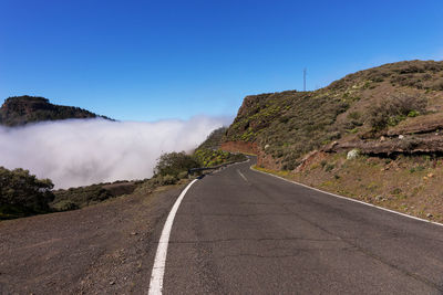 Road leading towards mountains against clear sky