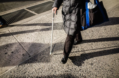 Low section of person walking on street with walking stick cane