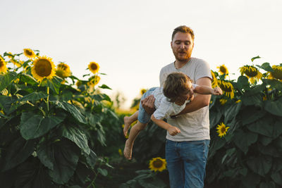 Father with little baby son in sunflowers field during golden hour. 