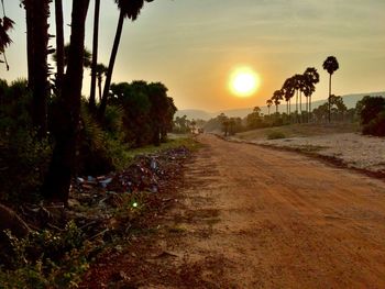 Road amidst trees against sky during sunset