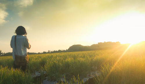 Rear view of boy standing on field against sky during sunset