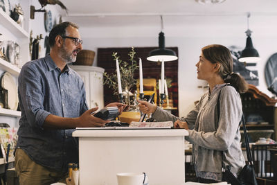 Owner giving credit card to female customer while standing at shop counter