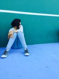 Full length of young woman sitting by green wall