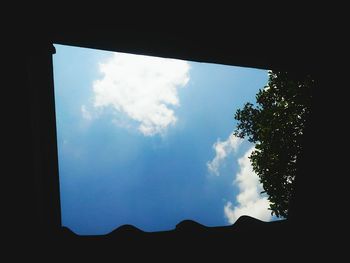 Low angle view of silhouette trees against blue sky seen through window