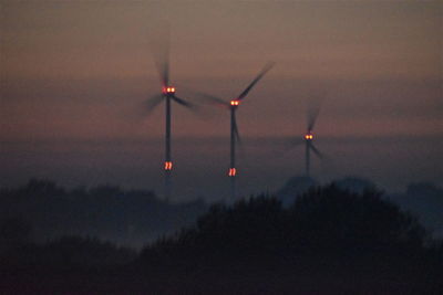 Silhouette wind turbines on field against sky at sunset