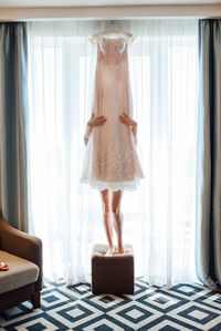 Low section of woman standing behind wedding dress indoors