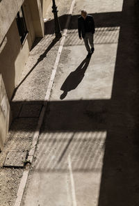 Man in black suit walking on path with sunlight and shadow