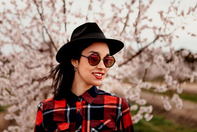 Woman wearing sunglasses and hat against pink flowers