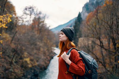 Young woman looking away while standing against trees during autumn