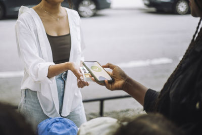 Woman doing online payment through mobile app while shopping at flea market