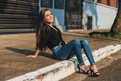 Full length of smiling young woman sitting on footpath