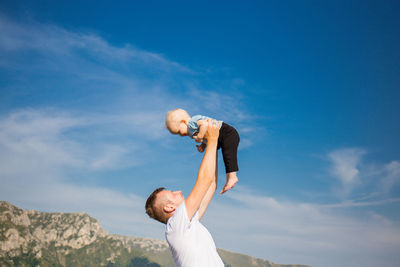 Man with arms raised standing against sky