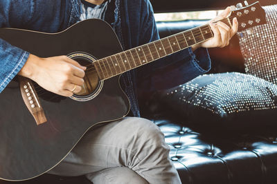 Midsection of man playing guitar at home