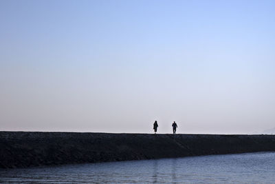 People walking at beach against clear sky