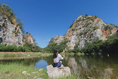 Woman sitting on rock by lake against sky