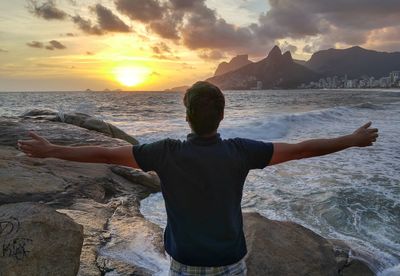 Rear view of man with arms outstretched standing at beach