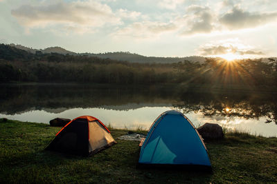 Tent by lake against sky during sunset