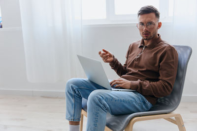 Young man using laptop while sitting on sofa at home