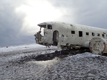 Abandoned airplane on snow covered land against sky