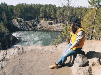 Rear view of woman sitting on rock by river