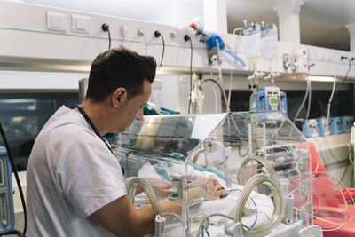 Doctor male attentively taking care of faceless newborn baby lying in incubator in clinic
