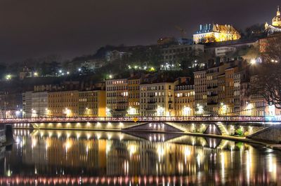 Illuminated city by river against sky at night