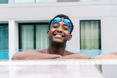 Young man with swimming goggles on his head and snorkeling leaning on the edge of a pool