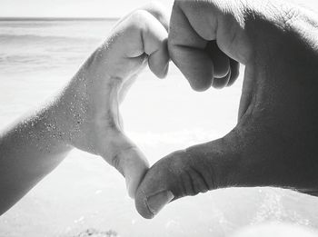 Cropped image of man and woman forming heart shape at beach