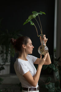 Woman gardener with natural makeup, holding a syngonium in glass flask in her green house