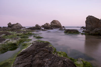 Rocks on beach against sky during sunset