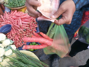 Close-up of man holding paper currency and carrots in plastic bag at market