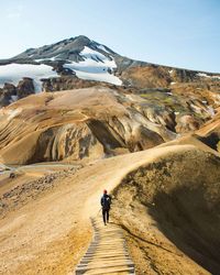 Rear view of man walking on mountain against sky